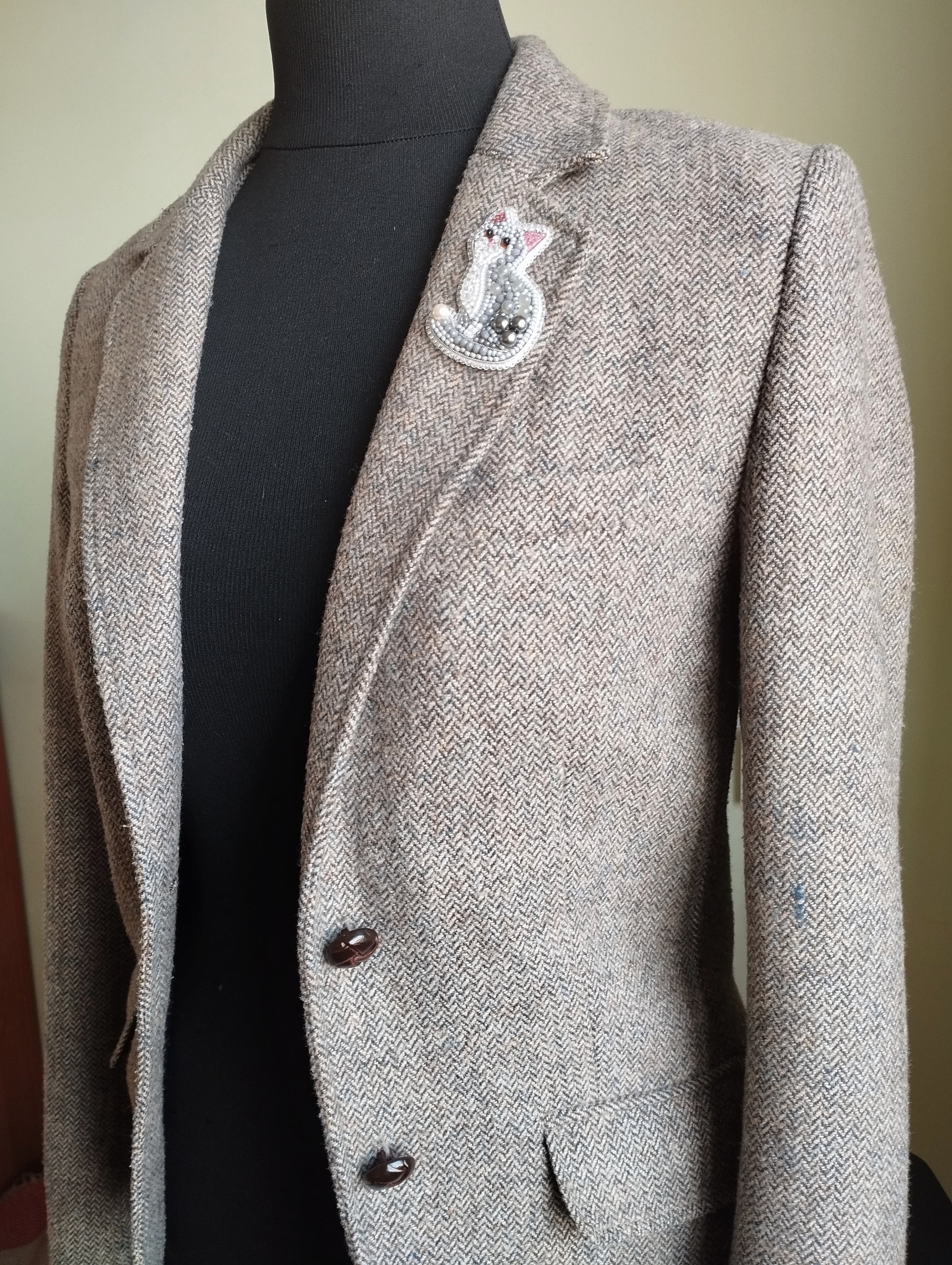 A gray tweed blazer with a decorative pin on the lapel.