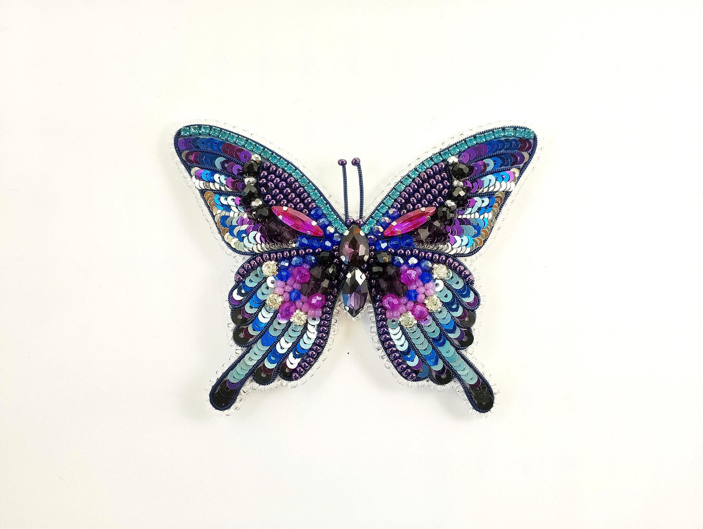 A colorful, intricately designed butterfly-shaped piece of jewelry made of sequins, beads, and other embellishments.