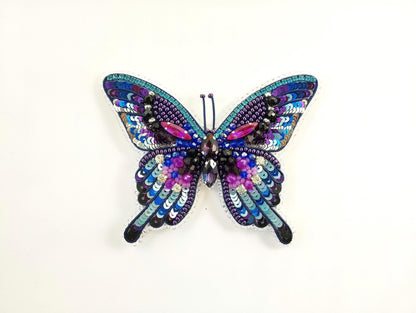 A colorful, intricately designed butterfly-shaped piece of jewelry made of sequins, beads, and other embellishments.