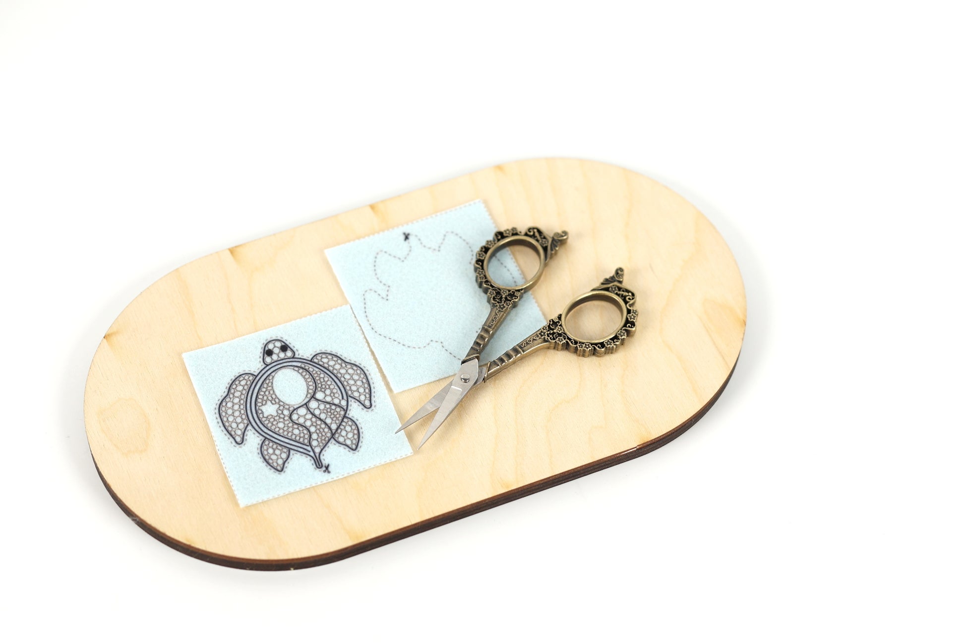 a pair of ornate scissors resting on a wooden board, with a piece of paper featuring a design on it.