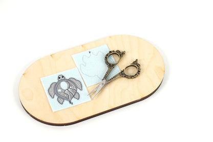 a pair of ornate scissors resting on a wooden board, with a piece of paper featuring a design on it.