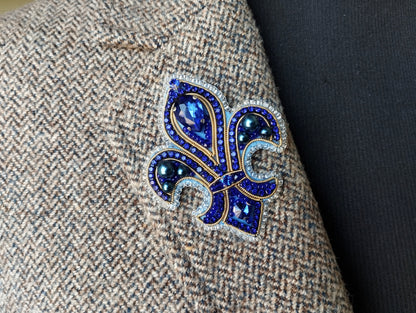 a close-up view of a decorative blue and gold brooch or pin, which is attached to a grey tweed fabric.