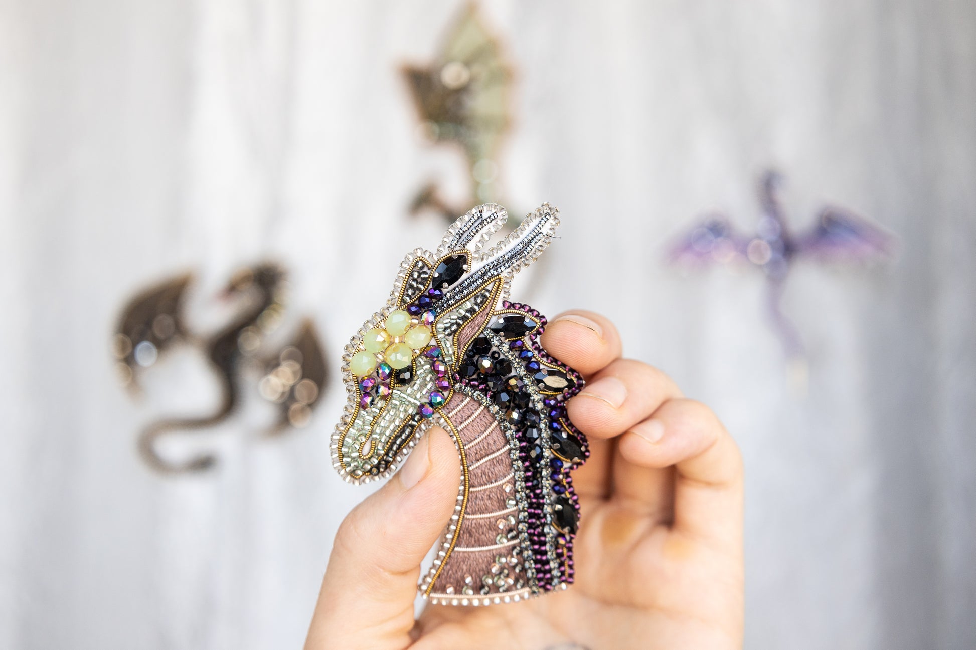 A hand holding a decorative dragon pin against a blurred background with other dragon-themed items.
