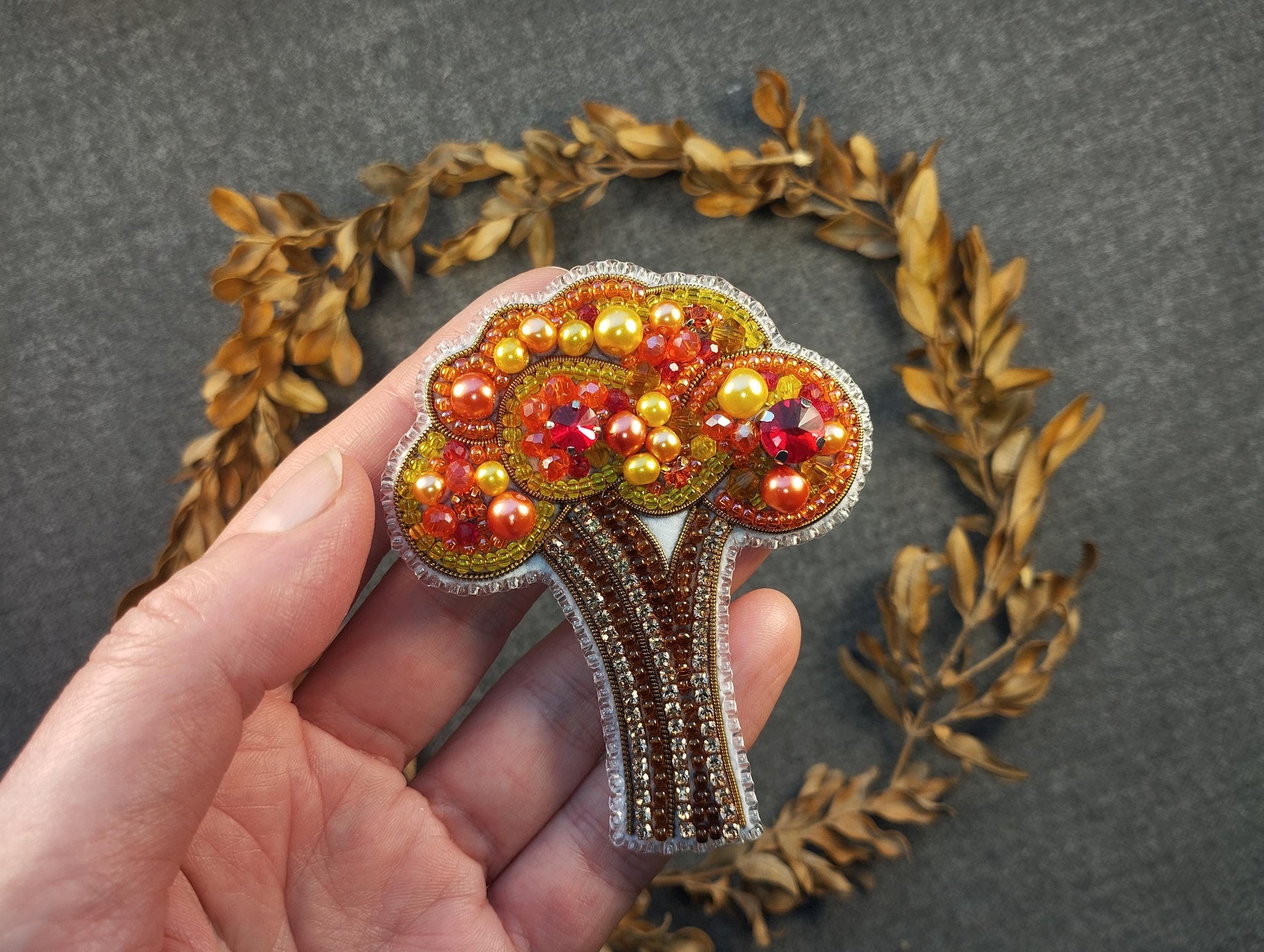 a hand holding a brooch with a tree on it