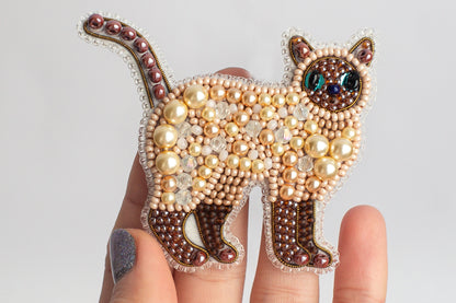 A hand holding a decorative cat pin made of beads and pearls.