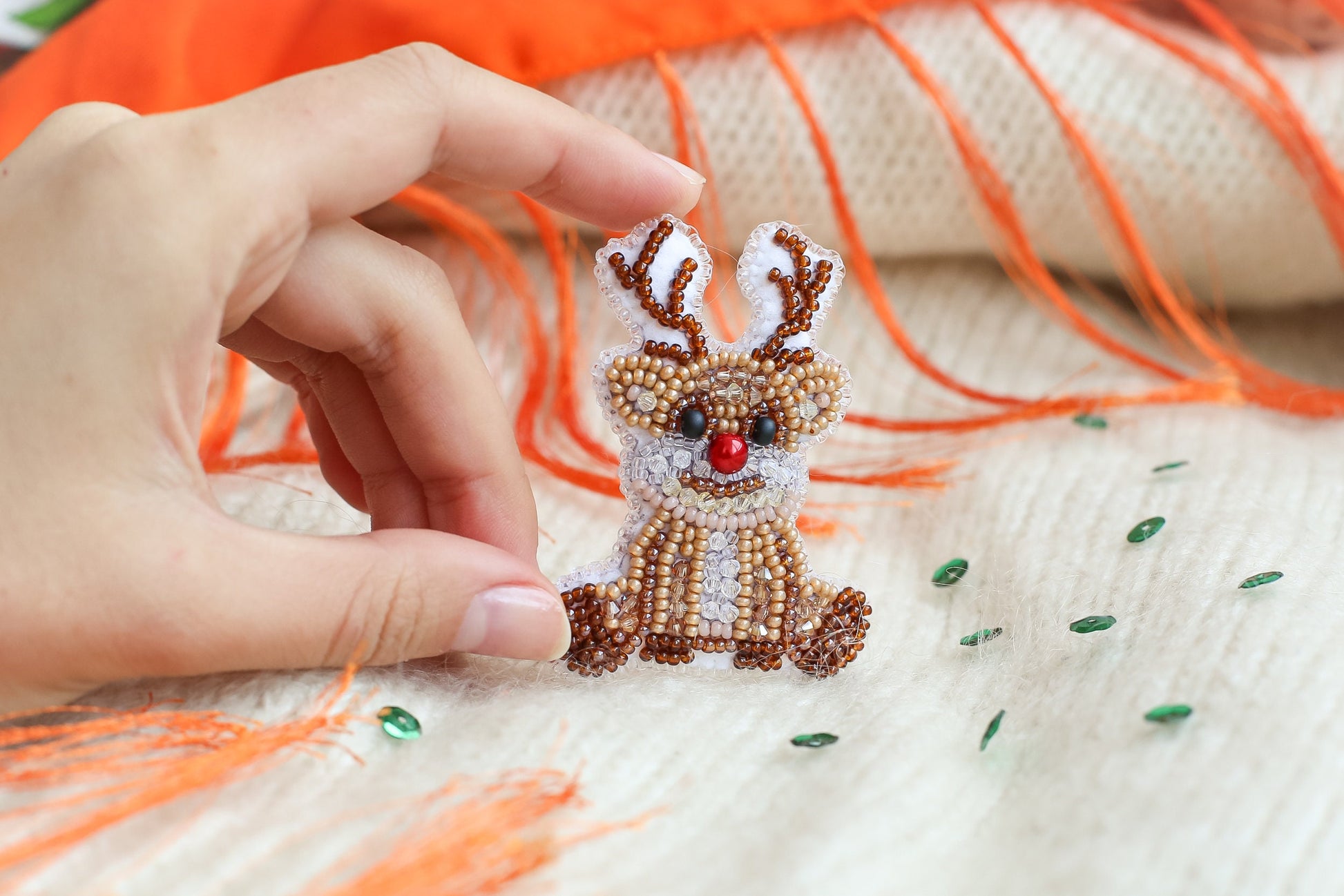 a hand is holding a beaded reindeer ornament