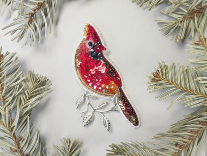 a red bird ornament hanging from a pine tree