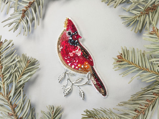 a red bird ornament hanging from a pine tree