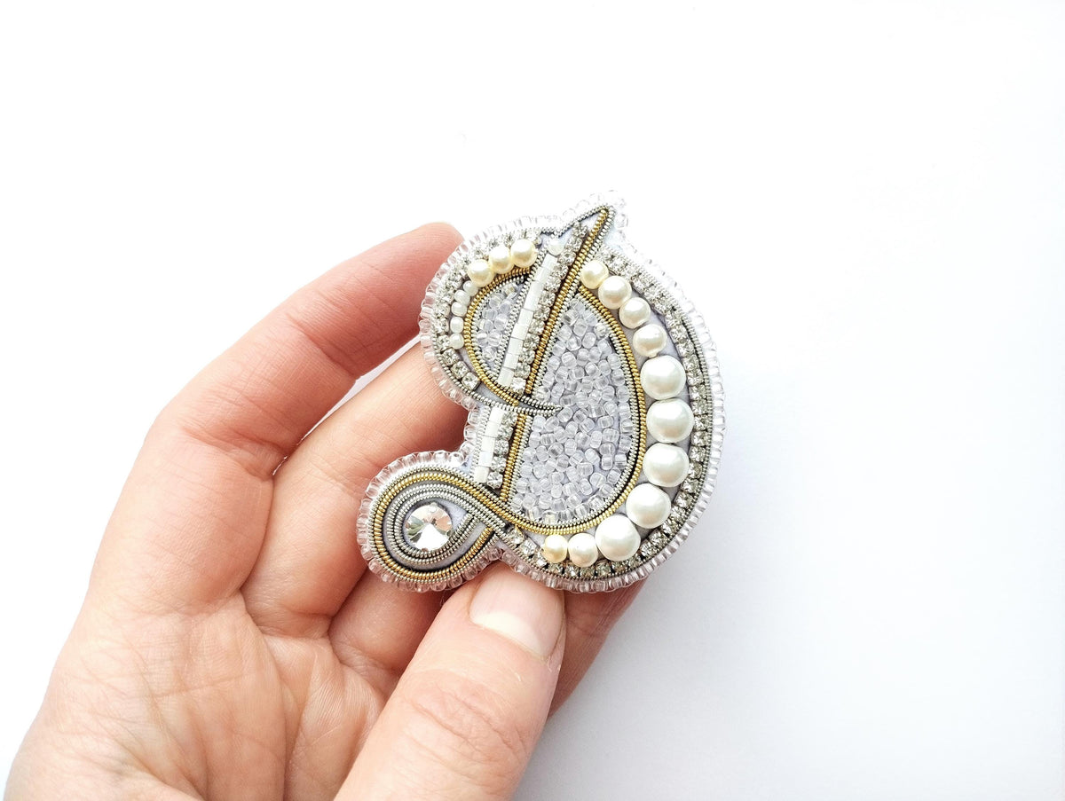 A hand holding a decorative letter D made of beads, pearls, and crystals.