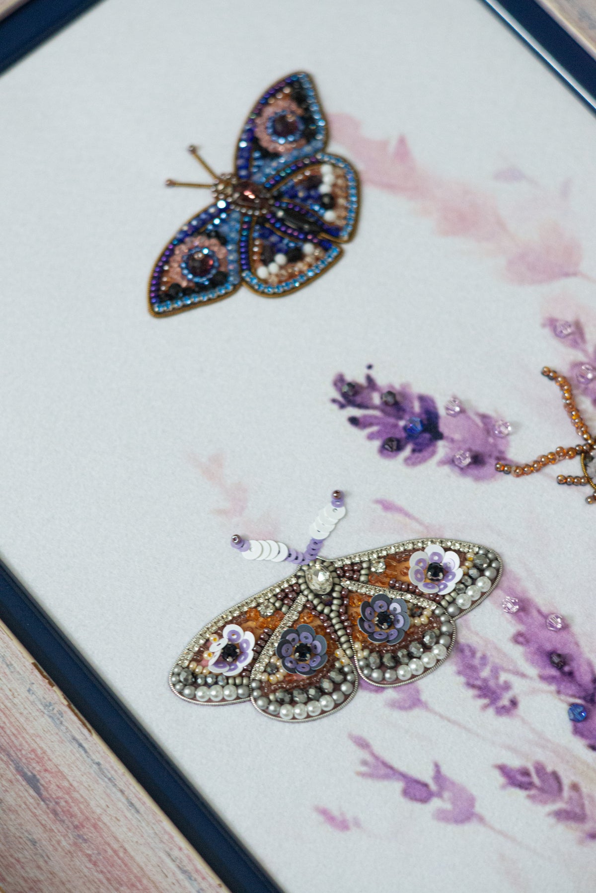 two intricately designed butterflies, one with a blue and gold color scheme and the other with a purple and gold color scheme, both adorned with sparkling embellishments.