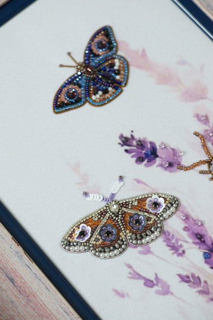 two intricately designed butterflies, one with a blue and gold color scheme and the other with a purple and gold color scheme, both adorned with sparkling embellishments.