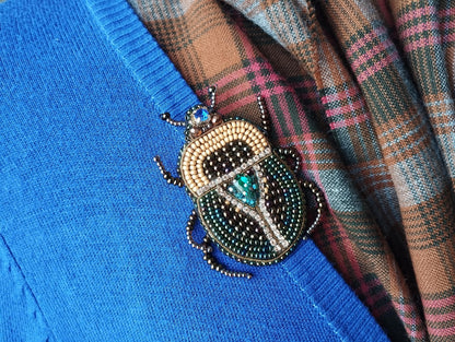 A close-up image of a blue sweater with a decorative beaded insect brooch pinned to it.