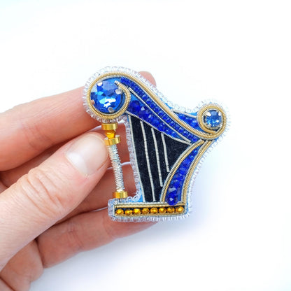 A hand holding a decorative piece featuring a blue and gold design with a central blue gemstone surrounded by smaller blue gemstones.