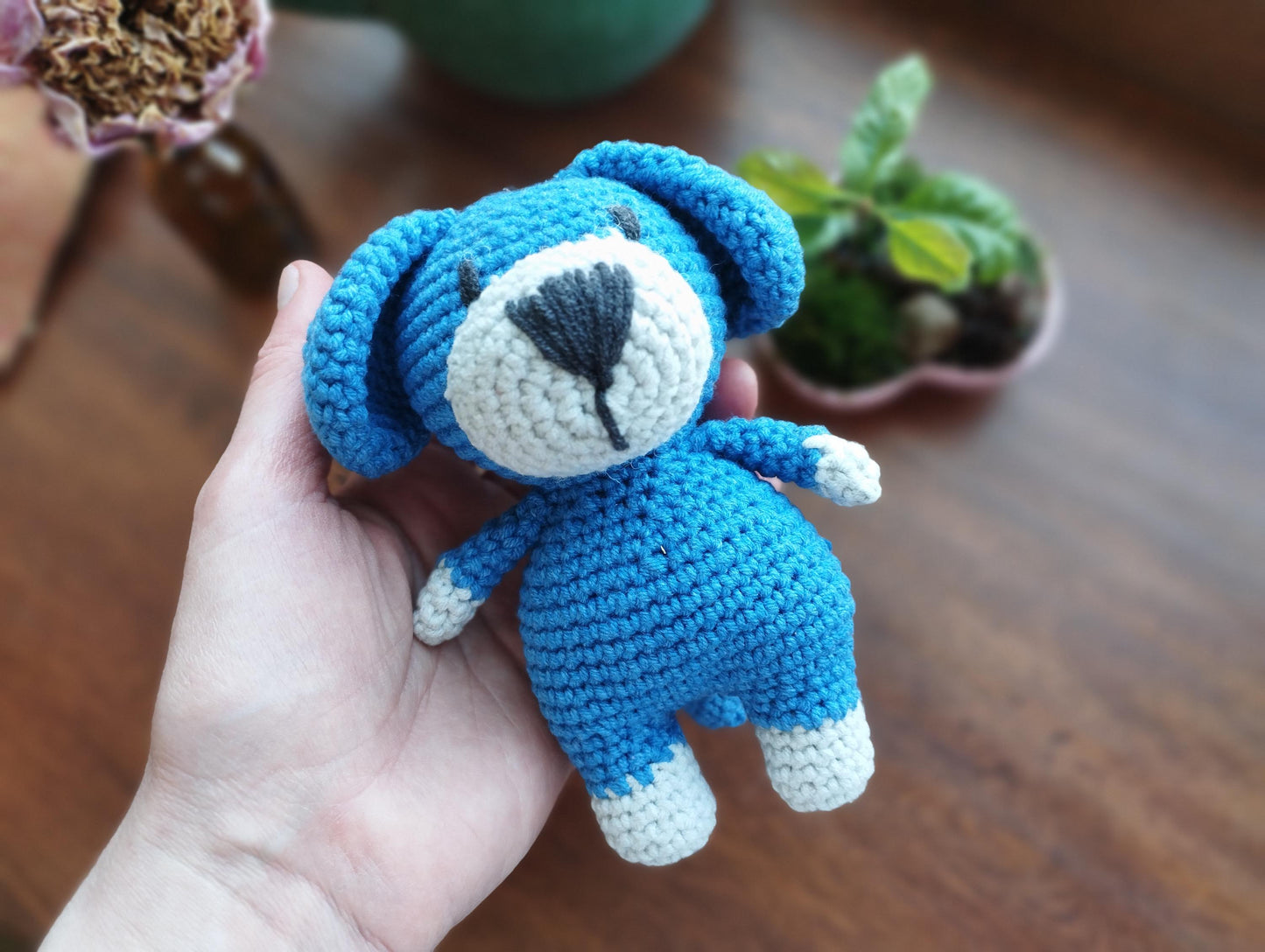 a hand holding a small crocheted blue teddy bear