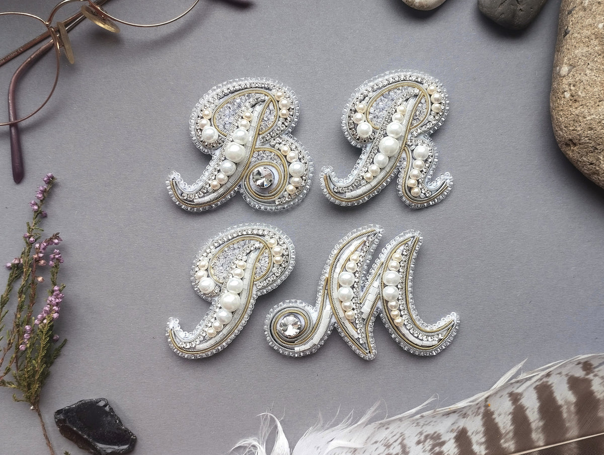 a collection of decorative elements, including a pair of ornate letters, a pair of glasses, and various natural elements such as feathers and stones, all arranged on a gray background.