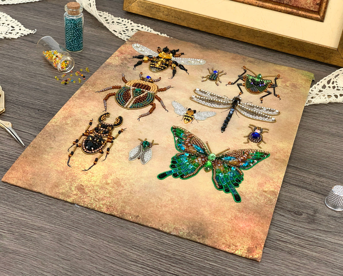 a collection of various insects, including a dragonfly, a bee, and several butterflies, arranged on a textured surface. There are also some beads and a small bottle of beads visible in the scene.