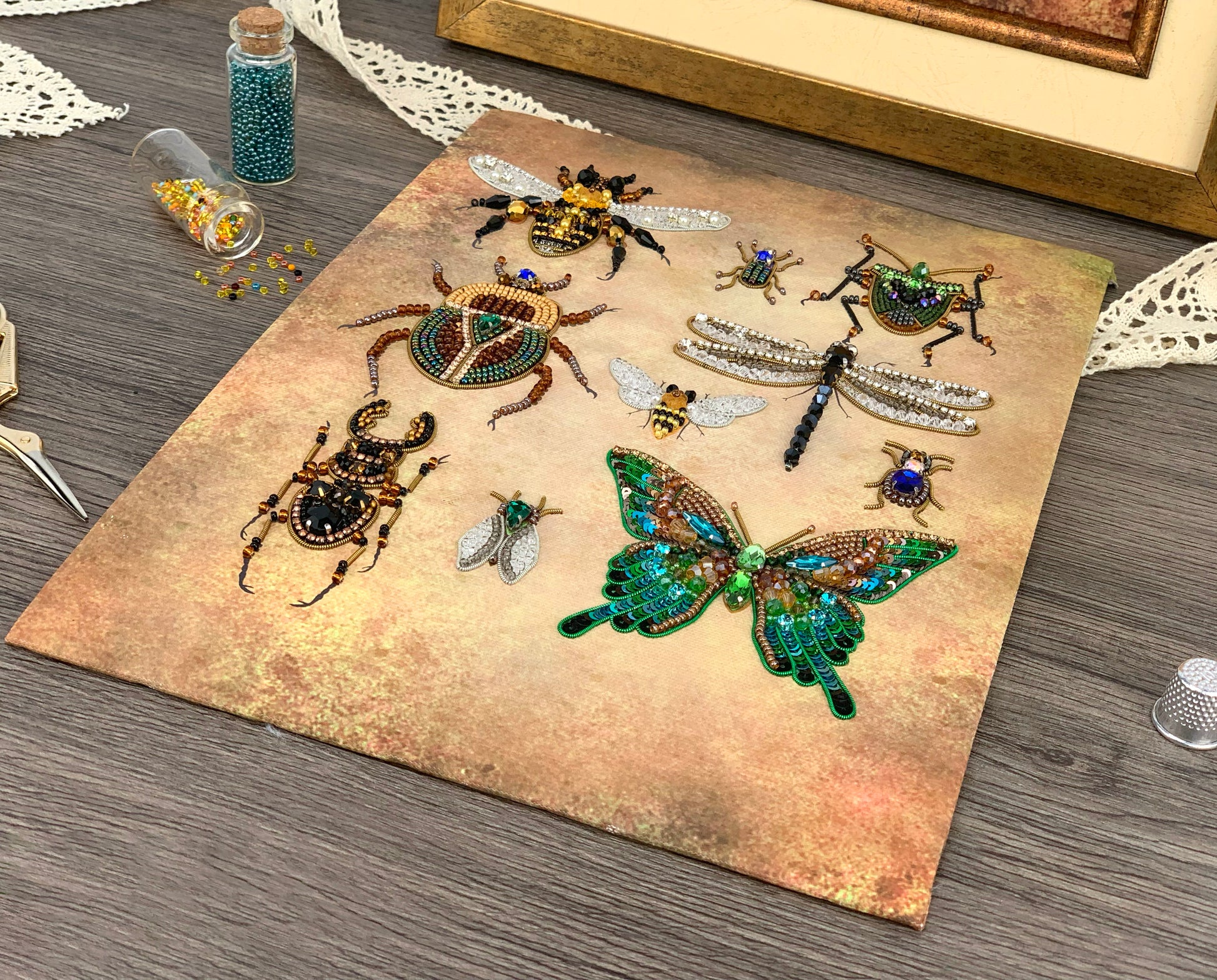 a collection of various insects, including a dragonfly, a bee, and several butterflies, arranged on a textured surface. There are also some beads and a small bottle of beads visible in the scene.