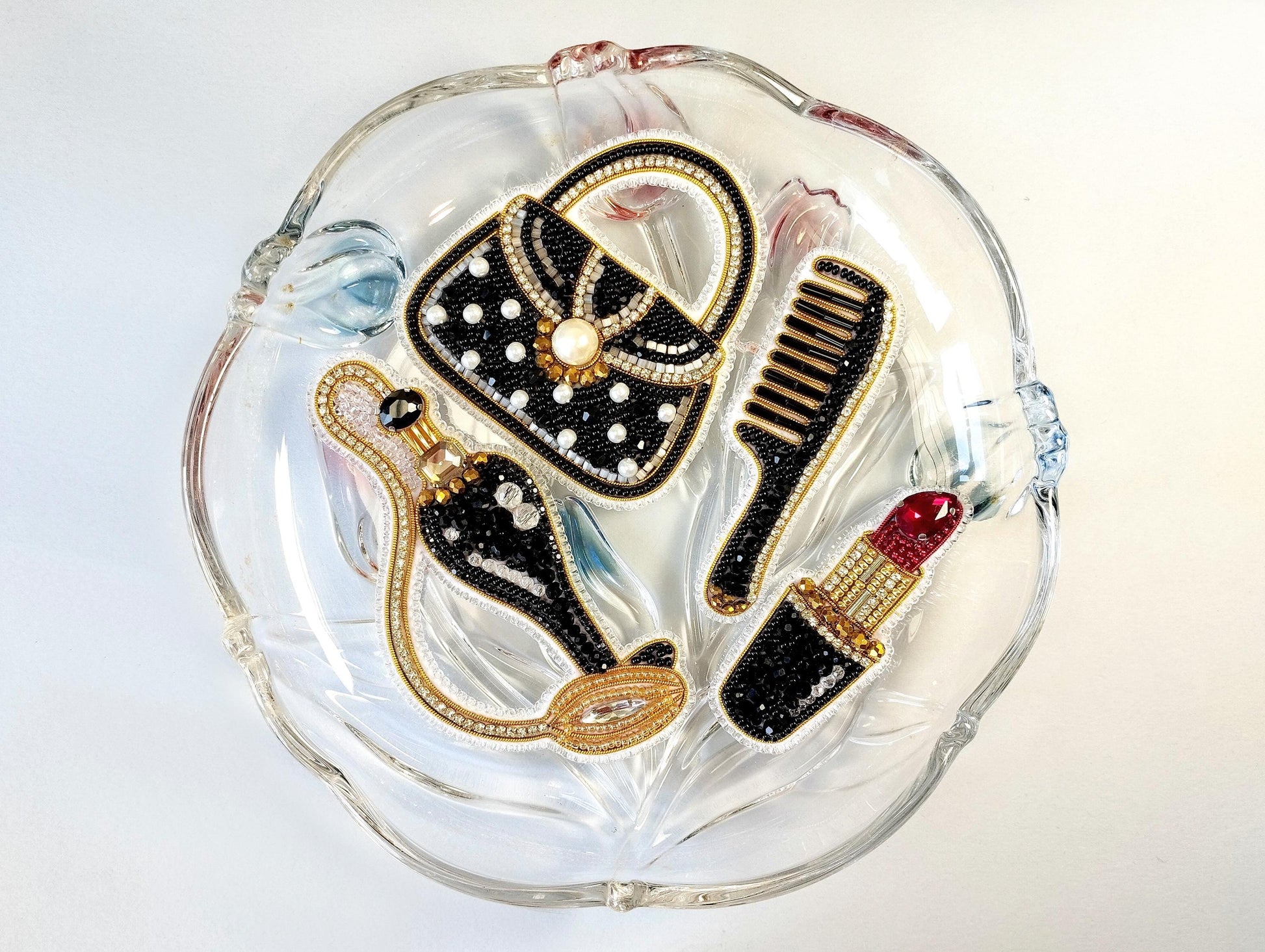 A glass plate with various decorative items, including a handbag, comb, and lipstick, arranged on it.