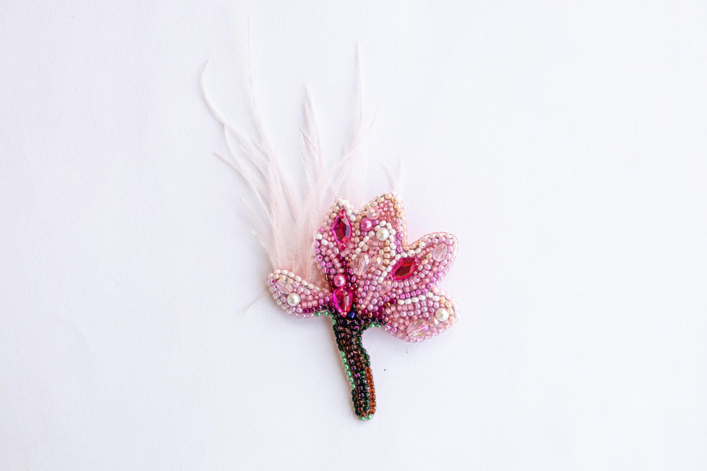 a pink flower with feathers on a white surface