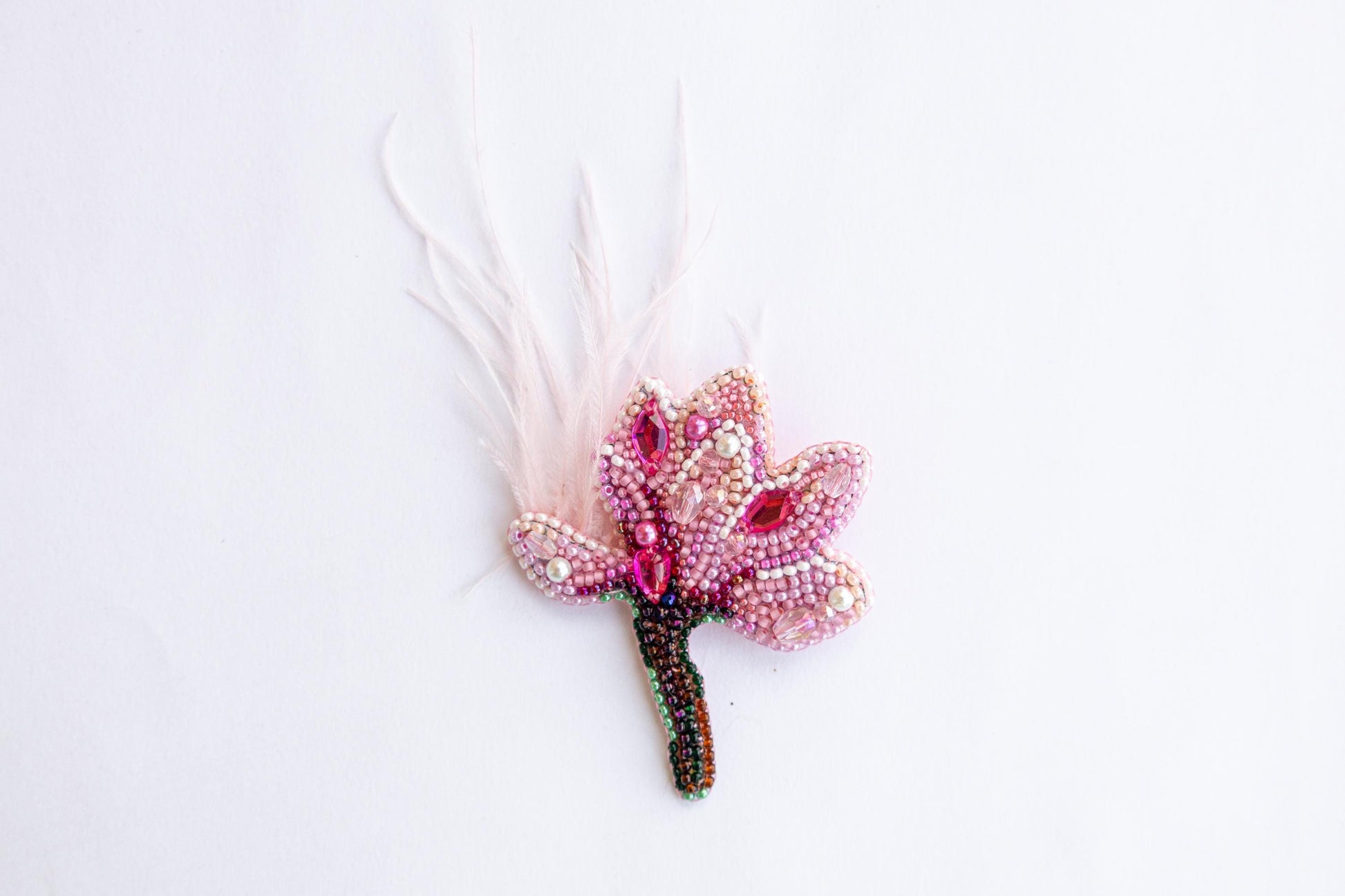 a pink flower with feathers on a white surface
