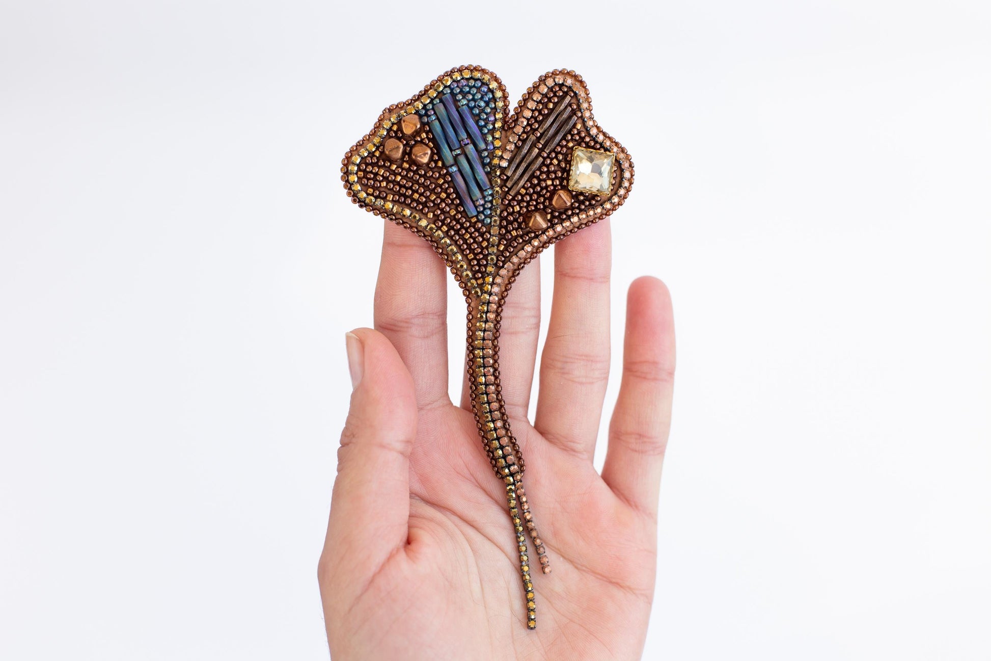 A hand holding a decorative piece of jewelry, which appears to be a beaded or woven accessory.