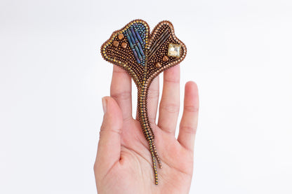 A hand holding a decorative piece of jewelry, which appears to be a beaded or woven accessory.