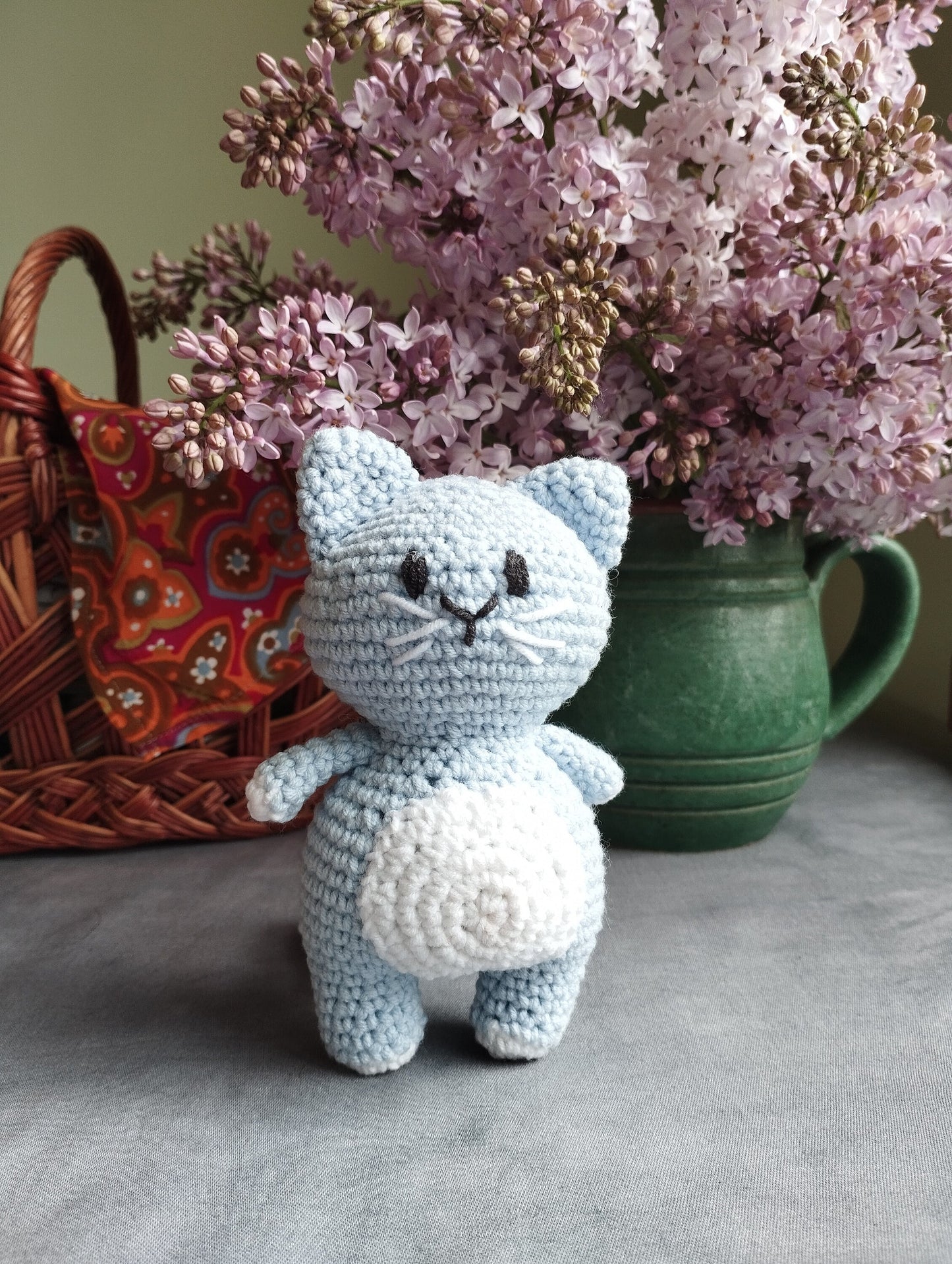 a crocheted cat sitting next to a vase of flowers