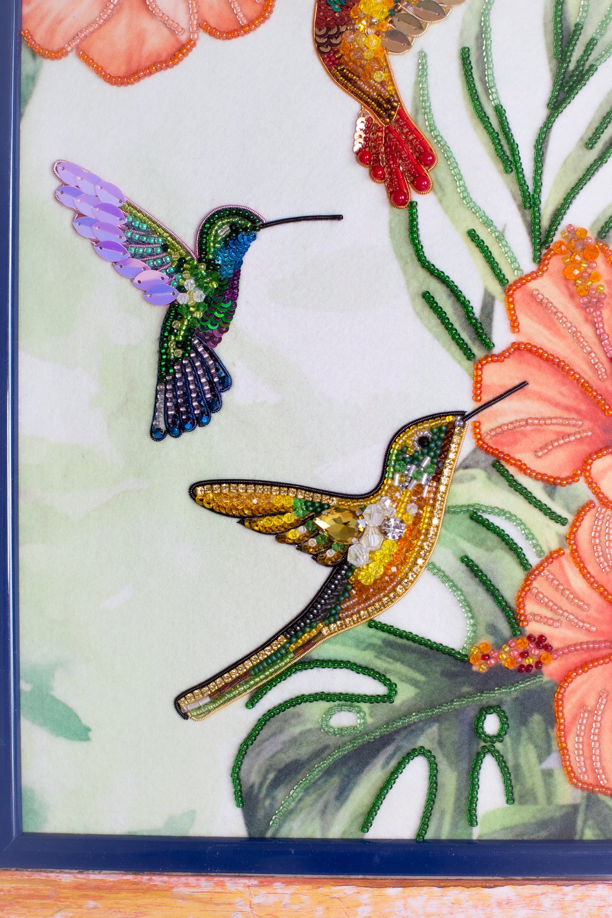 two colorful hummingbirds, one in purple and the other in yellow, against a backdrop of vibrant flowers and lush green leaves.