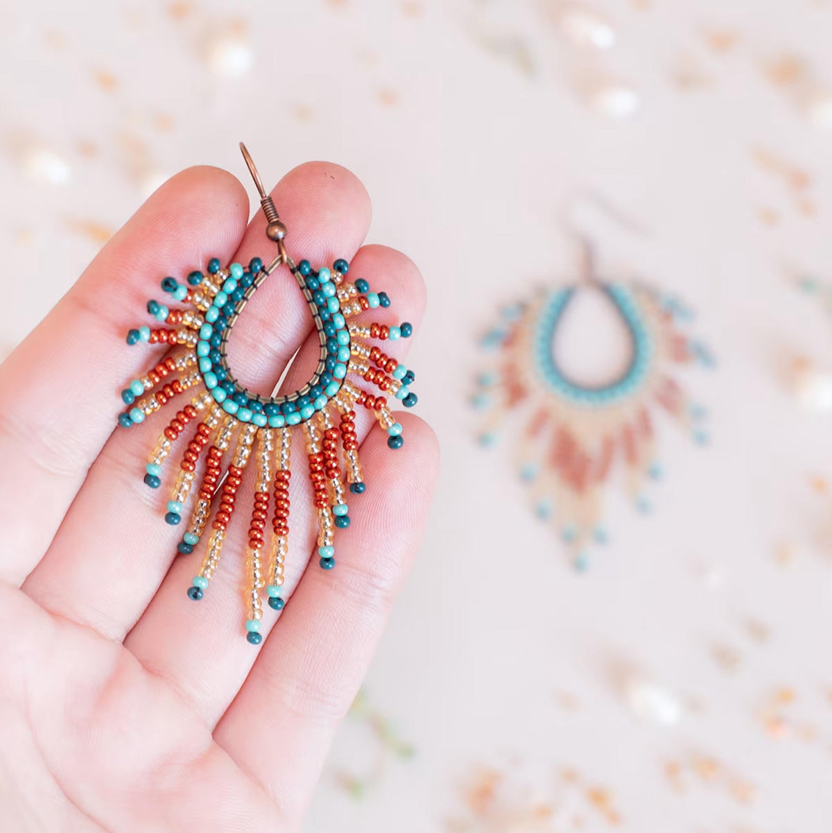 A hand holding a colorful beaded earring with a sunburst design.