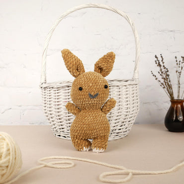 a small stuffed rabbit sitting in a basket next to a ball of yarn