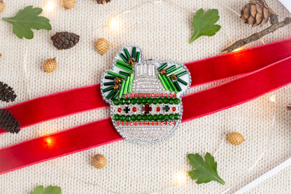 a decorative Christmas ornament with a red ribbon, surrounded by pine cones, leaves, and twinkling lights.