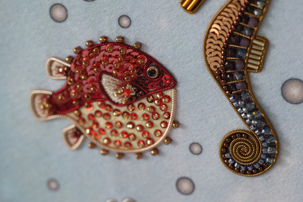 a close-up view of two decorative objects, one of which is a red and gold fish-shaped embroidery, and the other is a gold and blue spiral-shaped object.