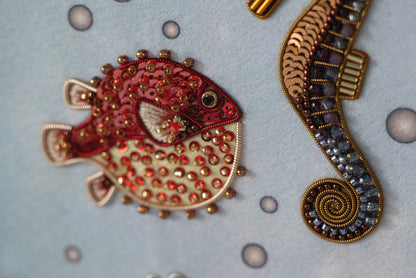 a close-up view of two decorative objects, one of which is a red and gold fish-shaped embroidery, and the other is a gold and blue spiral-shaped object.