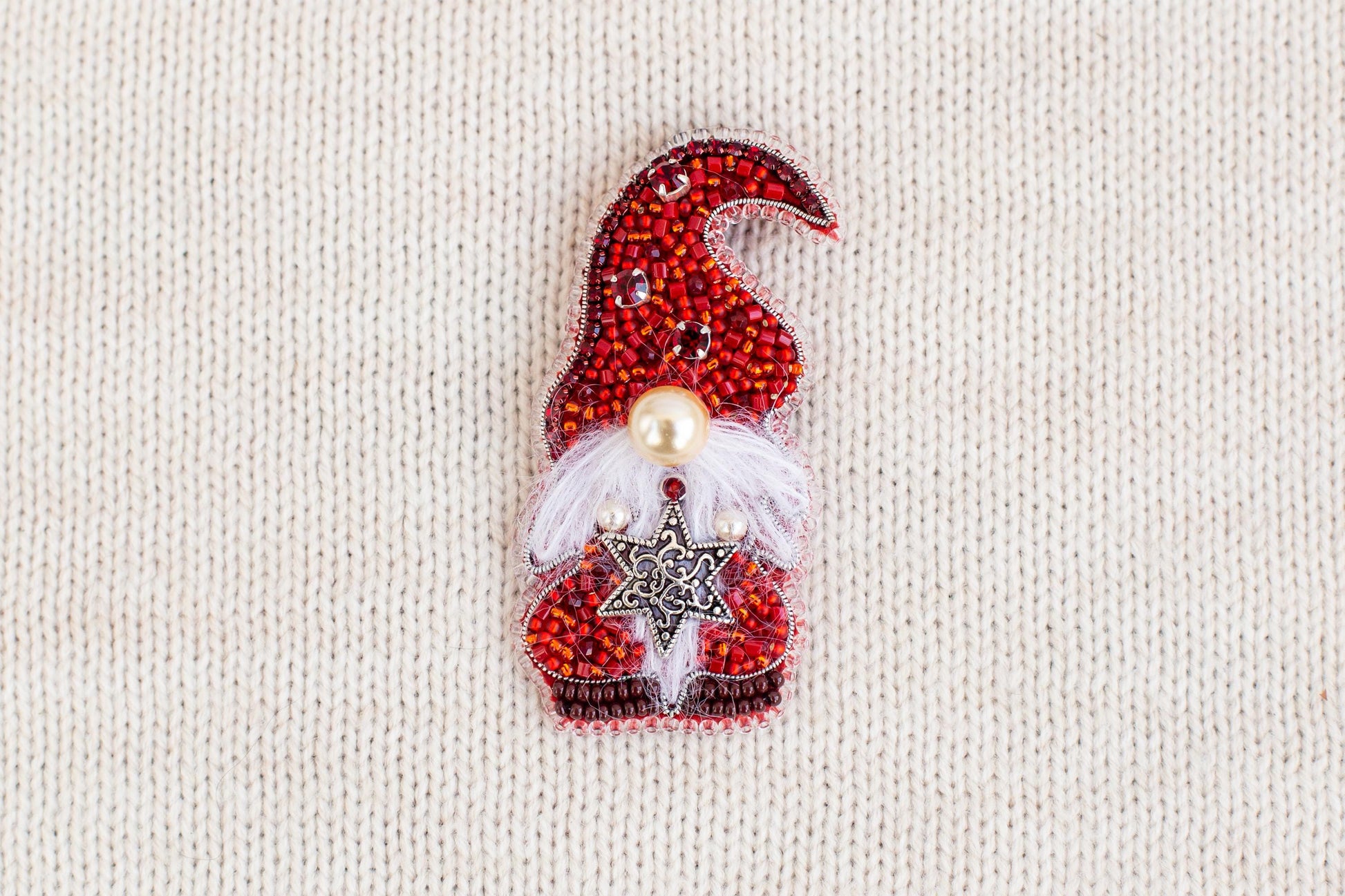 A red and white knitted ornament with a star and a pearl, resembling a gnome or Christmas-themed decoration, is displayed on a white background.