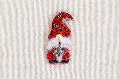 A red and white knitted ornament with a star and a pearl, resembling a gnome or Christmas-themed decoration, is displayed on a white background.