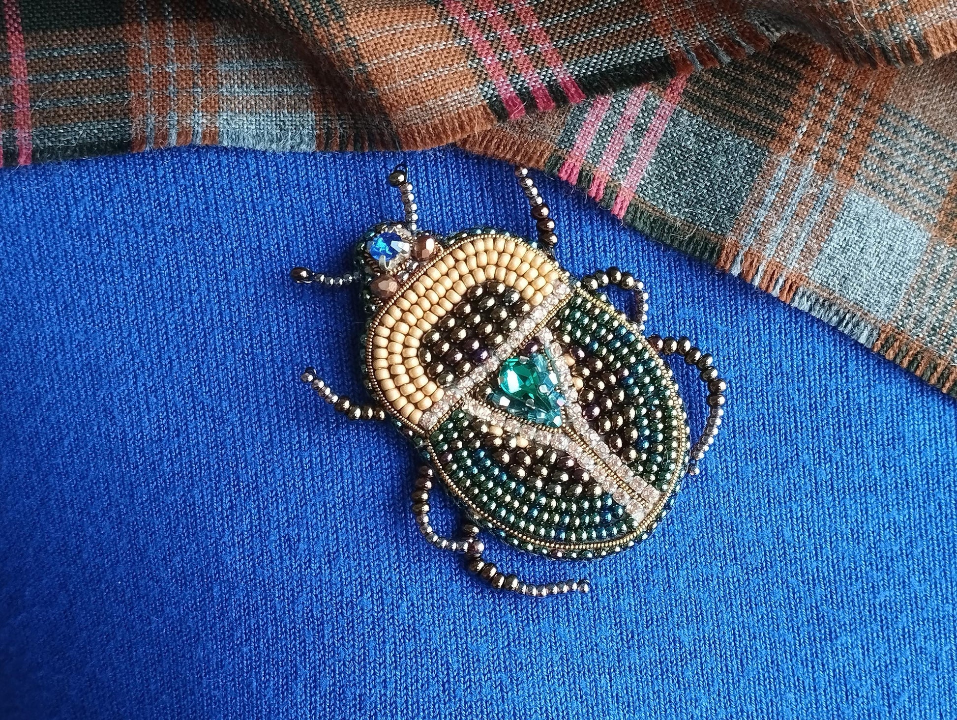 A close-up image of a decorative beaded insect, possibly a ladybug or a similar type of insect, on a blue fabric background.