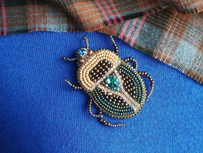 A close-up image of a decorative beaded insect, possibly a ladybug or a similar type of insect, on a blue fabric background.