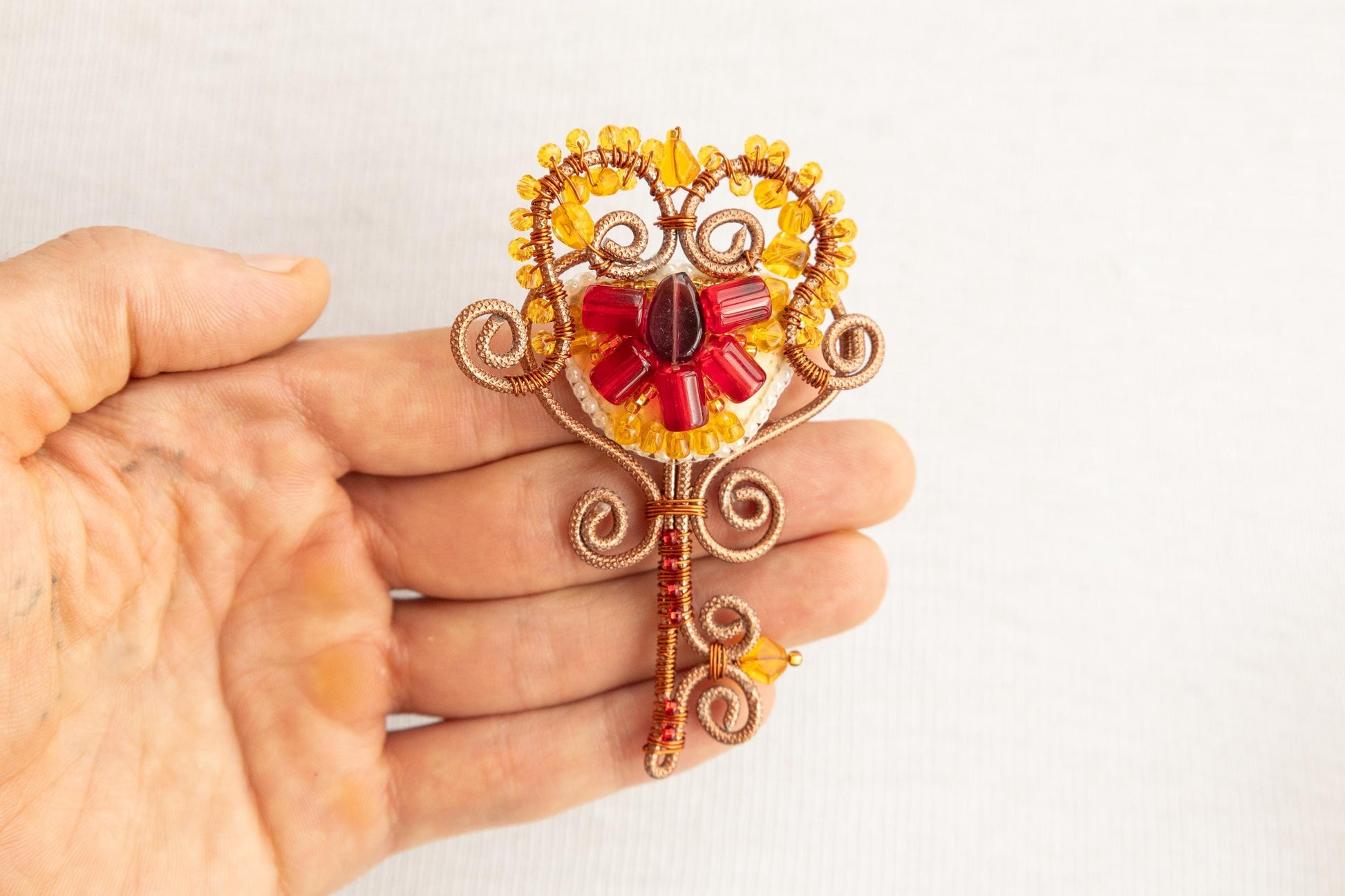 a hand holding a brooch with a red flower on it