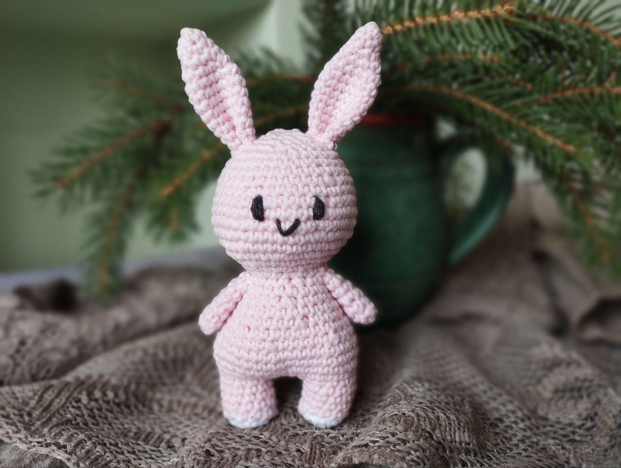 a pink crocheted bunny sitting next to a pine tree