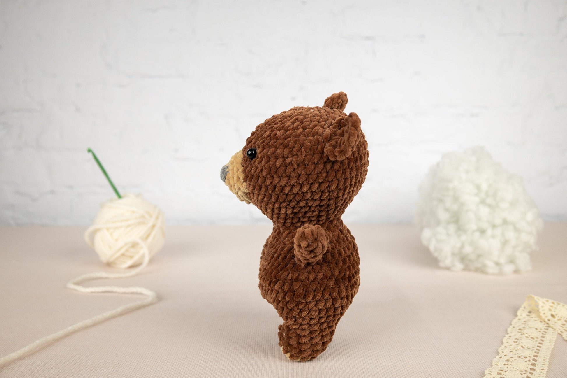 a brown teddy bear standing next to a ball of yarn