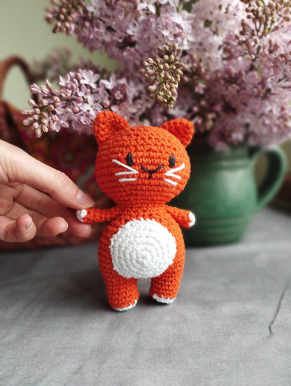 a crocheted cat sitting next to a vase of flowers