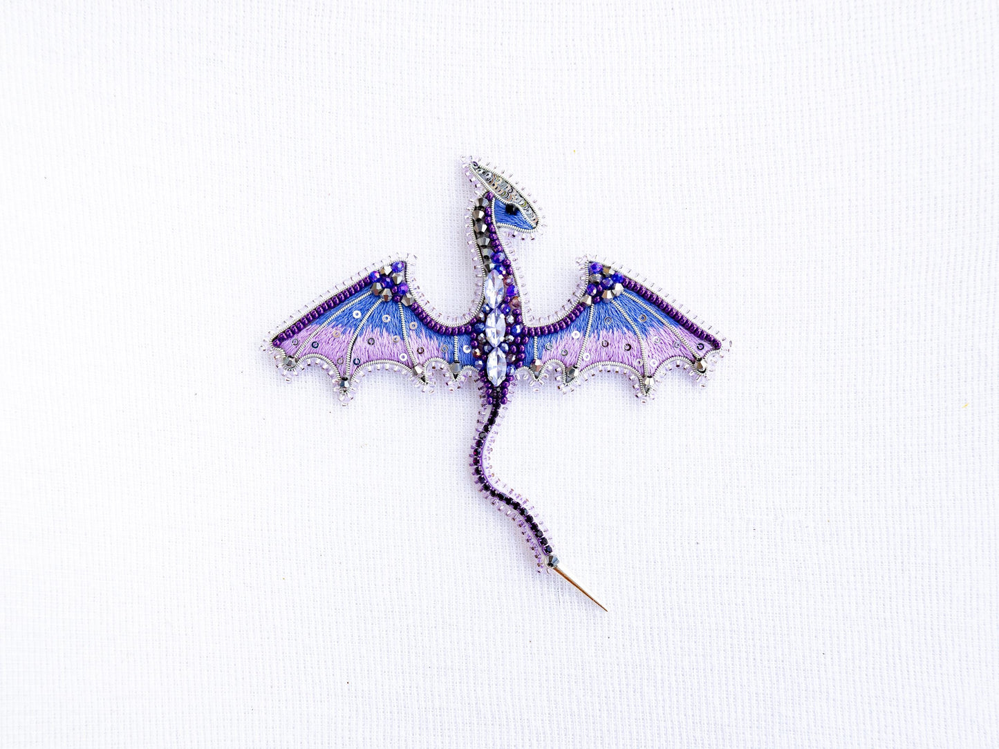 a purple and blue dragon brooch sitting on top of a white surface