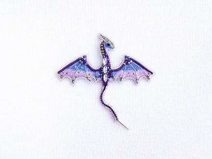 a purple and blue dragon brooch sitting on top of a white surface