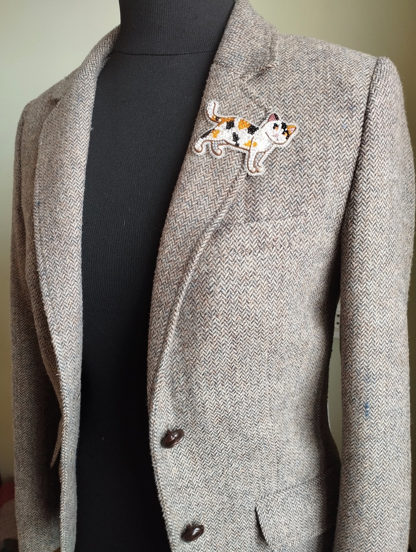 A gray tweed jacket with a black turtleneck sweater underneath, and a decorative cat embroidered patch on the left breast area.