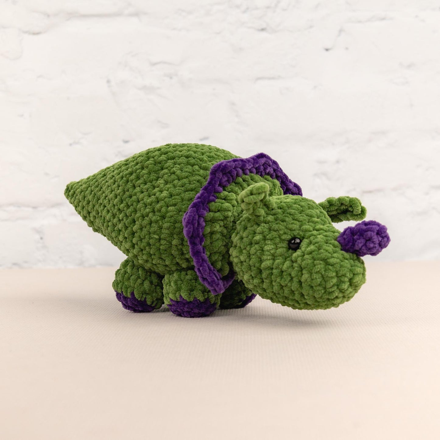 a crocheted green stuffed animal with a purple ribbon around its neck