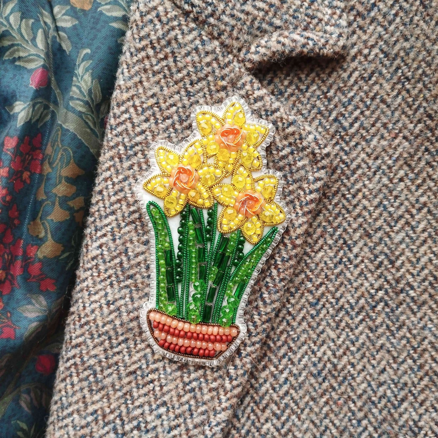 A close-up of a decorative fabric with a floral pattern and a beaded embroidered flower design on the left side.