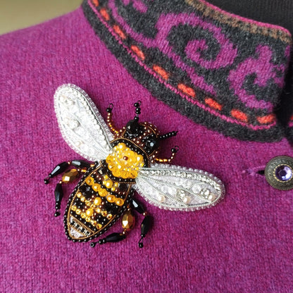 A close-up image of a decorative beaded bee pin on a purple sweater.