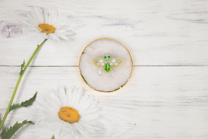 a bee brooch sitting on top of a white table next to daisies