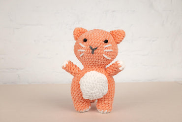 a crocheted orange cat holding a white ball