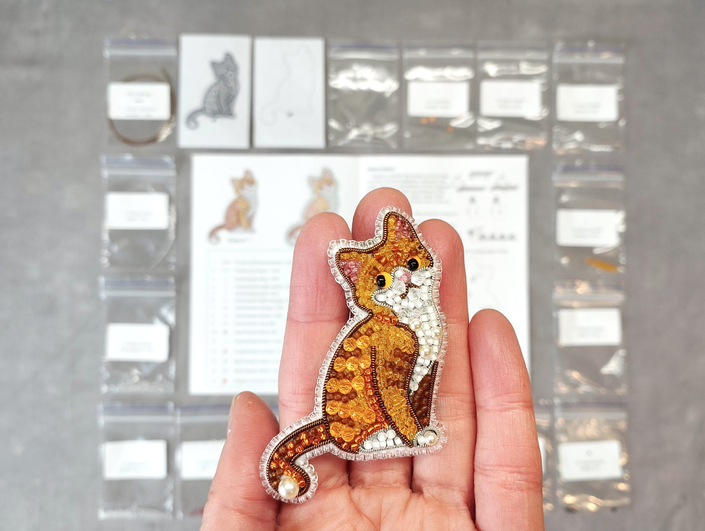 A hand holding a small, intricately beaded cat pin.